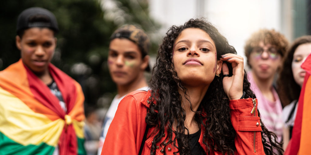 Five young, diverse individuals, some draped in the pride flag, pose for the camera